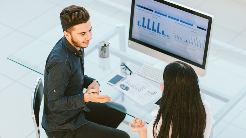 Two employees reviewing Google Demand Gen campaign data at an office desk for a paid ads strategy discussion
